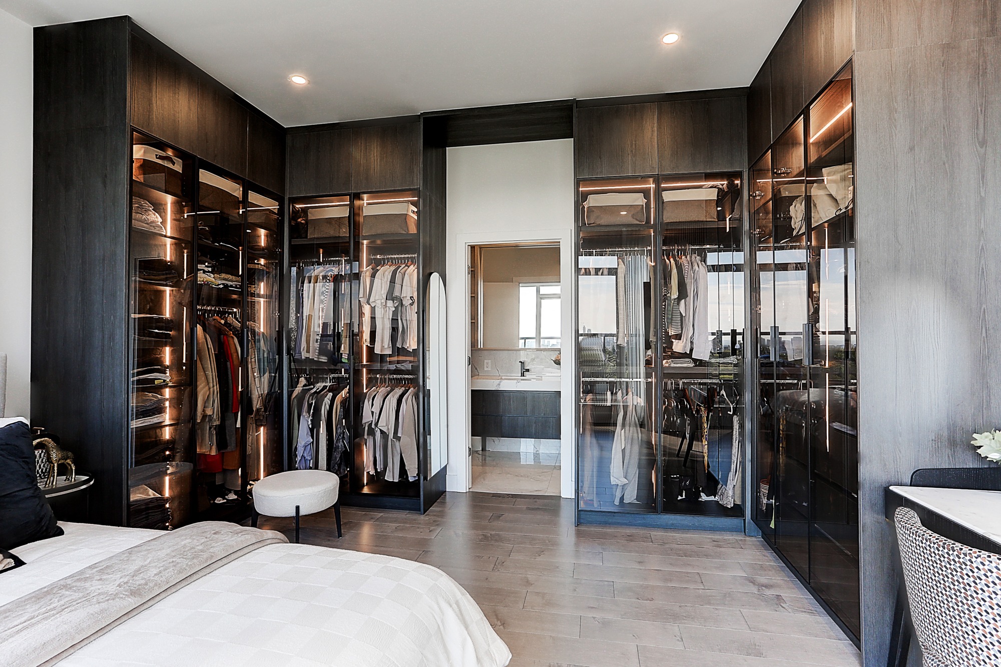 Glass-front wardrobe walls with interior lighting in a Toronto condo bedroom